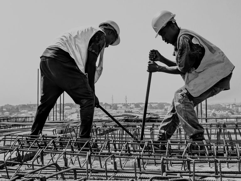 Black and white image of two construction workers reinforcing steel bars on a building site.